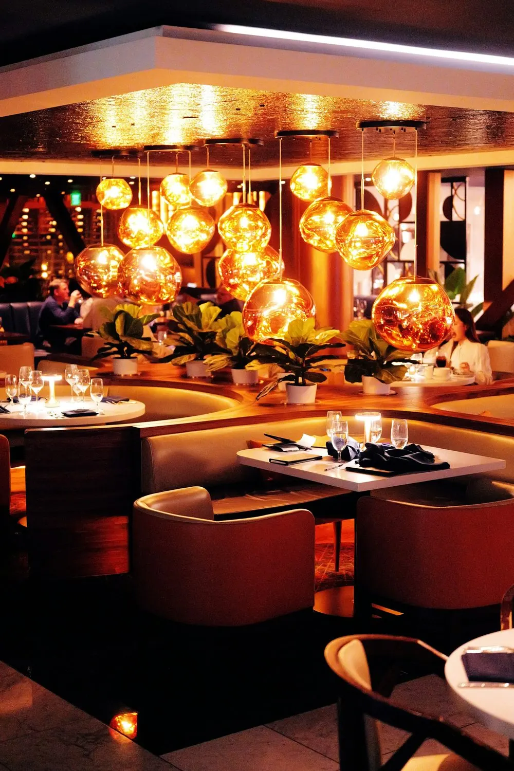 Restaurant dining room with booths and set tables under warm pendant lights