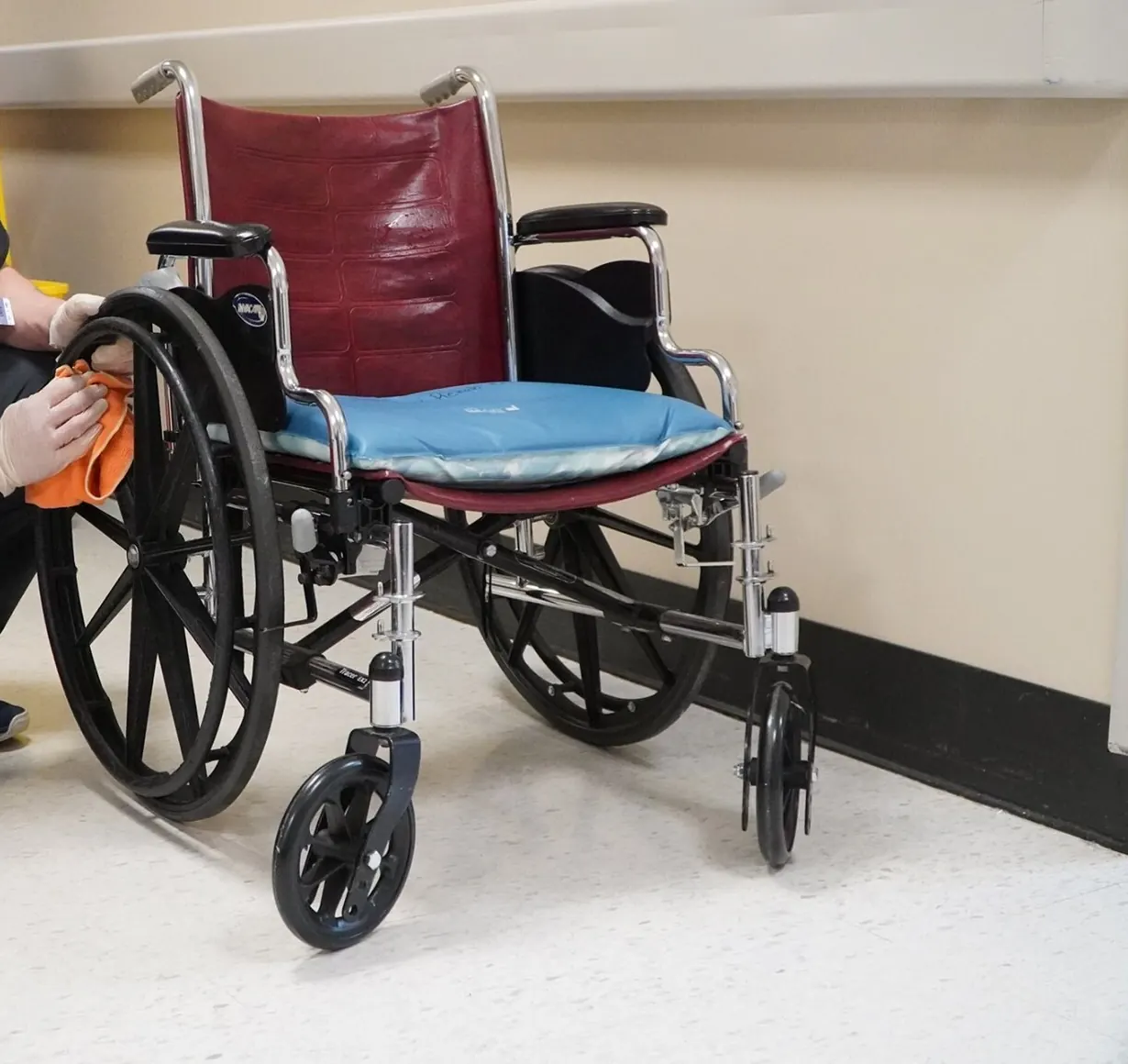 Gloved hands wiping down a wheelchair in a care facility hallway