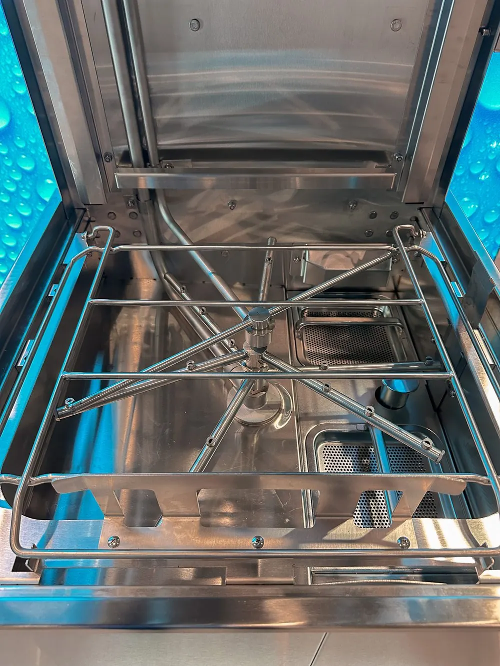 Inside a commercial dishwasher, showing the wash arms and rack guide